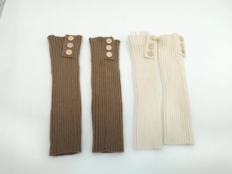 Zwei Paare gerippter Strick-Beinstulpen mit Holzknöpfen am oberen Rand, eine in Taupe und eine in Creme, flach photographiert auf weißem Untergrund