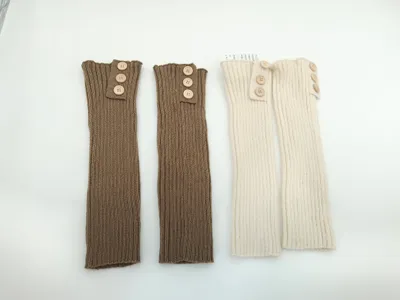 Zwei Paare gerippter Strick-Beinstulpen mit Holzknöpfen am oberen Rand, eine in Taupe und eine in Creme, flach photographiert auf weißem Untergrund