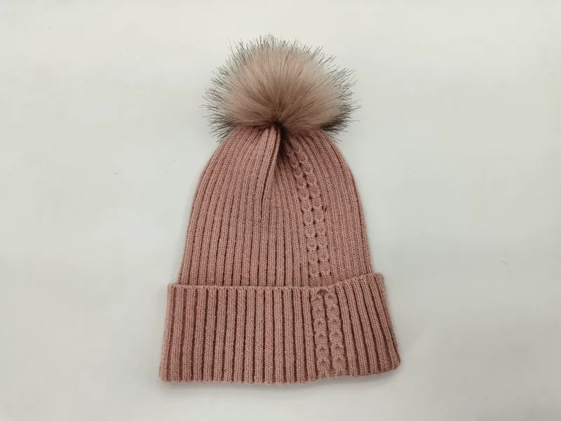 Puderrosa Strickmütze mit großem fluffigem Kunstfell-Pompom, auf weißem Hintergrund fotografiert