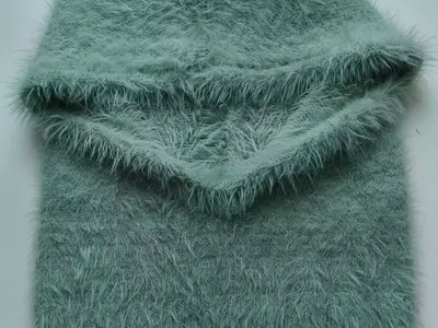 Gefaltete mintgrüne Flauschgarn-Balaclava mit passendem Schlauchschal auf weißem Hintergrund, Eyelash-Yarn-Textur sichtbar