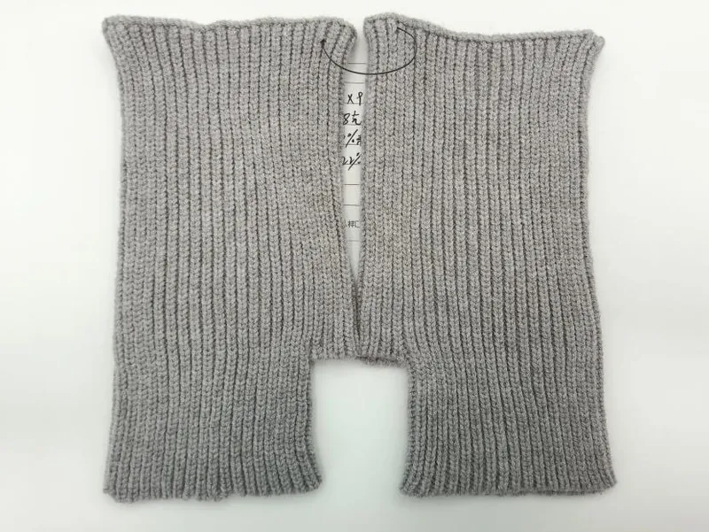 Ein Paar hellgraue fingerlose Strickhandschuhe mit Rippenmuster, flach liegend auf weißem Hintergrund, offene Fingeröffnungen gut sichtbar