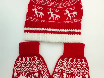 Rot-weiße Fair-Isle-Strickmütze mit Bommel und dazu passende Rentier-Handschuhe auf weißem Hintergrund