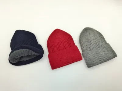 Drei gerippte Strickmützen in Dunkelblau, Rot und Grau auf weißem Hintergrund, Marineblaue Mütze zeigt graues Fleece-Innenfutter