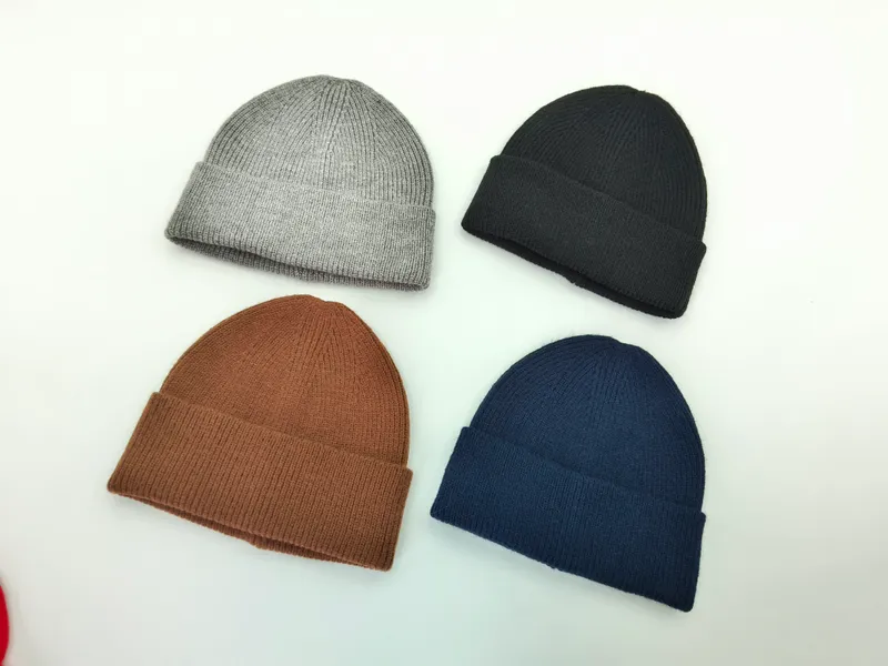 Vier gerippte Strickmützen mit Umschlagbündchen in Grau, Schwarz, Braun und Dunkelblau, flach photographiert auf weißem Hintergrund