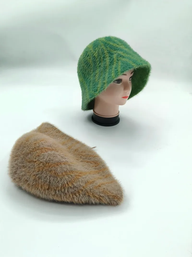 Grün gestreifter flauschiger Strick-Sonnenhut auf einer Hutform zusammen mit einem beigefarbenen flachen Strickhut auf weißem Untergrund