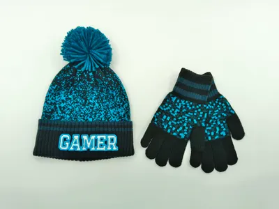 Kinder-Strickmütze in Petrol und Schwarz mit Bommel und dazu passende Pixel-Muster-Handschuhe auf weißem Hintergrund