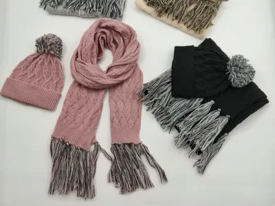 Vier Zopfstrick-Mützen-Schal-Sets in Grau, Creme, Rosa und Schwarz mit Bommel-Beanies und Fransen-Schals, flach ausgelegt