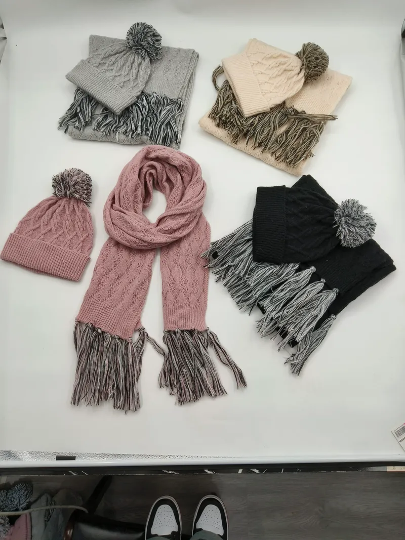 Vier Zopfstrick-Mützen-Schal-Sets in Grau, Creme, Rosa und Schwarz mit Bommel-Beanies und Fransen-Schals, flach ausgelegt