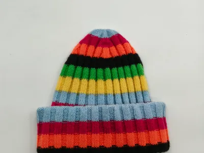 Bunte Strickmütze mit Umschlagrand in leuchtenden Streifen – Blau, Rosa, Orange, Schwarz, Grün und Gelb auf weißem Hintergrund