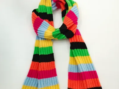 Langer Strickschal mit breiten bunten Querstreifen in Grün, Gelb, Orange, Pink, Blau und Schwarz auf hellem Untergrund