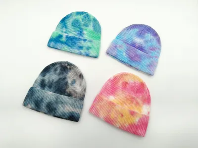 Vier Strickmützen im Batikfärbe-Look in den Farbtönen Blau-Grün, Lila-Blau, Dunkelgrau und Pink-Gelb vor weißem Hintergrund