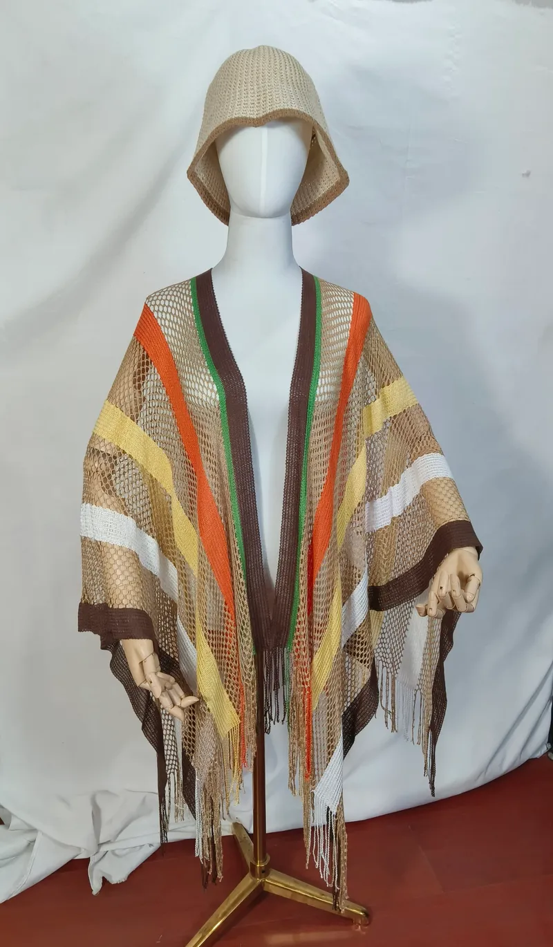 Schaufensterpuppe trägt einen braun-orange-gelben Netz-Poncho mit langen Fransen und passenden beigen Webe-Bucket Hat