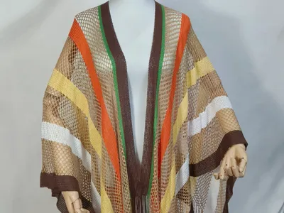 Schaufensterpuppe trägt einen braun-orange-gelben Netz-Poncho mit langen Fransen und passenden beigen Webe-Bucket Hat