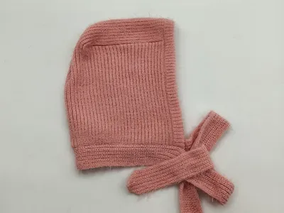 Weiche rosa Rippenstrick-Babyhaube mit langen Bindebändern, flach auf weißem Hintergrund
