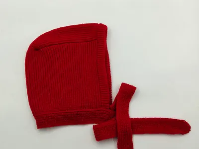 Rote gestrickte Babyhaube mit langen Bindebändern zum Binden unter dem Kinn, flach auf weißem Hintergrund