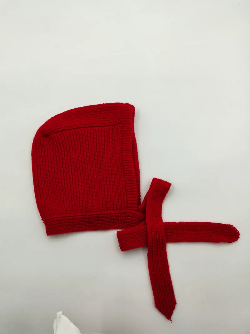 Rote gestrickte Babyhaube mit langen Bindebändern zum Binden unter dem Kinn, flach auf weißem Hintergrund
