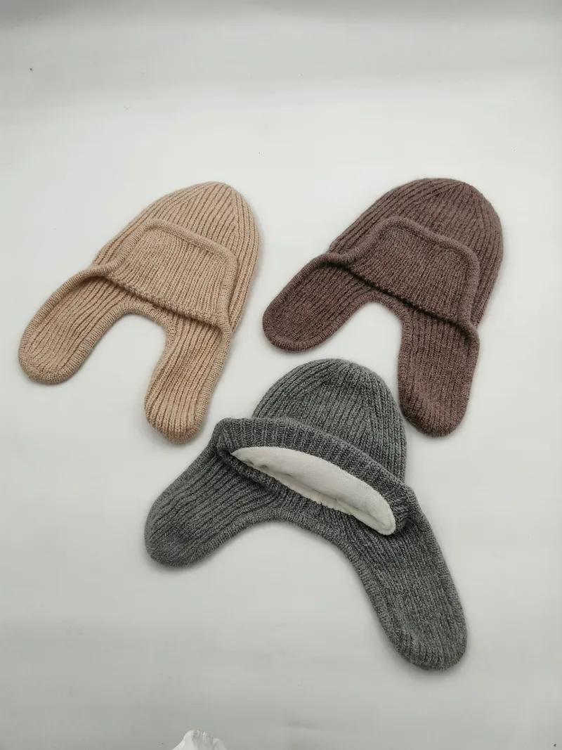 Drei Rippenstrick-Mützen mit seitlichen Ohrklappen in Beige, Braun und Grau nebeneinander auf weißem Hintergrund
