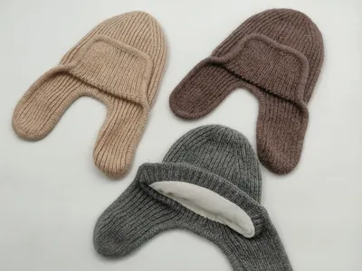 Drei Rippenstrick-Mützen mit seitlichen Ohrklappen in Beige, Braun und Grau nebeneinander auf weißem Hintergrund