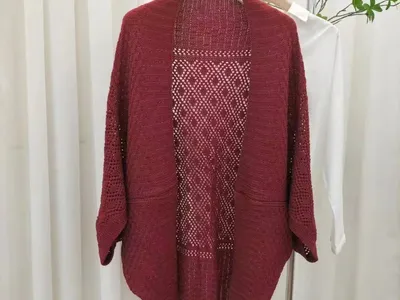 Burgunderrote offene Strickjacke mit Rautenspitzen-Häkelrücken und Dreiviertelärmeln auf einem Kleiderständer