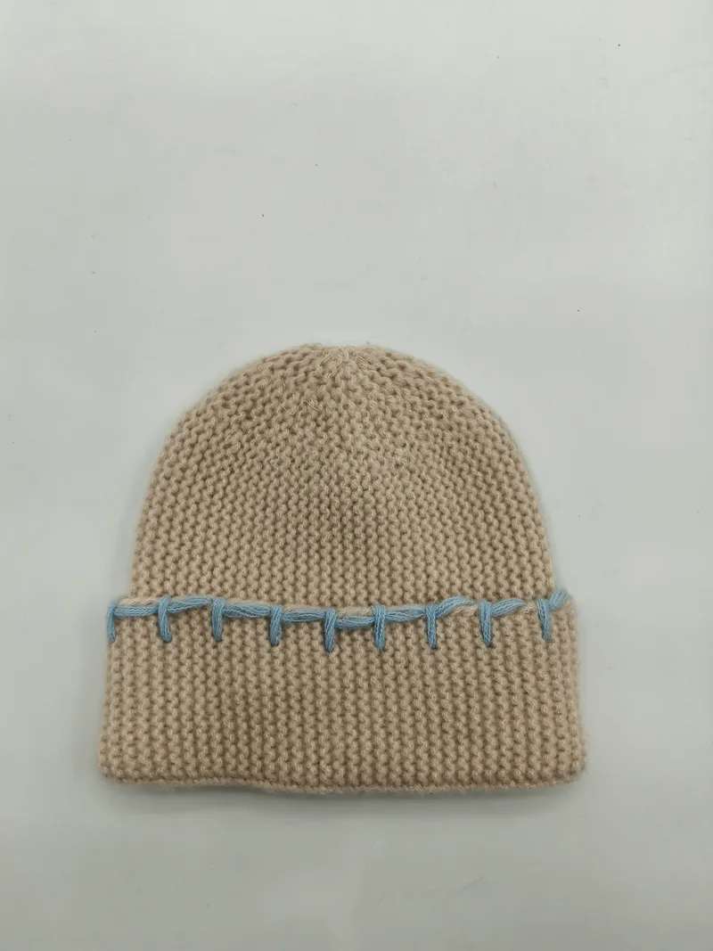 Cremefarbene Wintermütze aus dickem Garn mit auffälliger blauer Kontrastnaht entlang des gefalteten Randes, Studioaufnahme