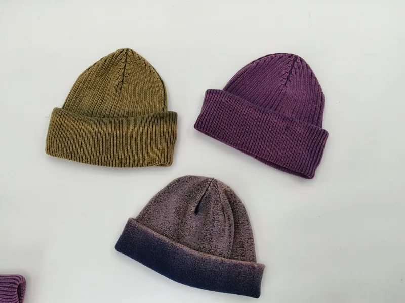 Drei zusammengelegte Rippstrickmützen in Olivgrün, gedämpftem Violett und zweifarbigem Grau-Dunkelblau nebeneinander