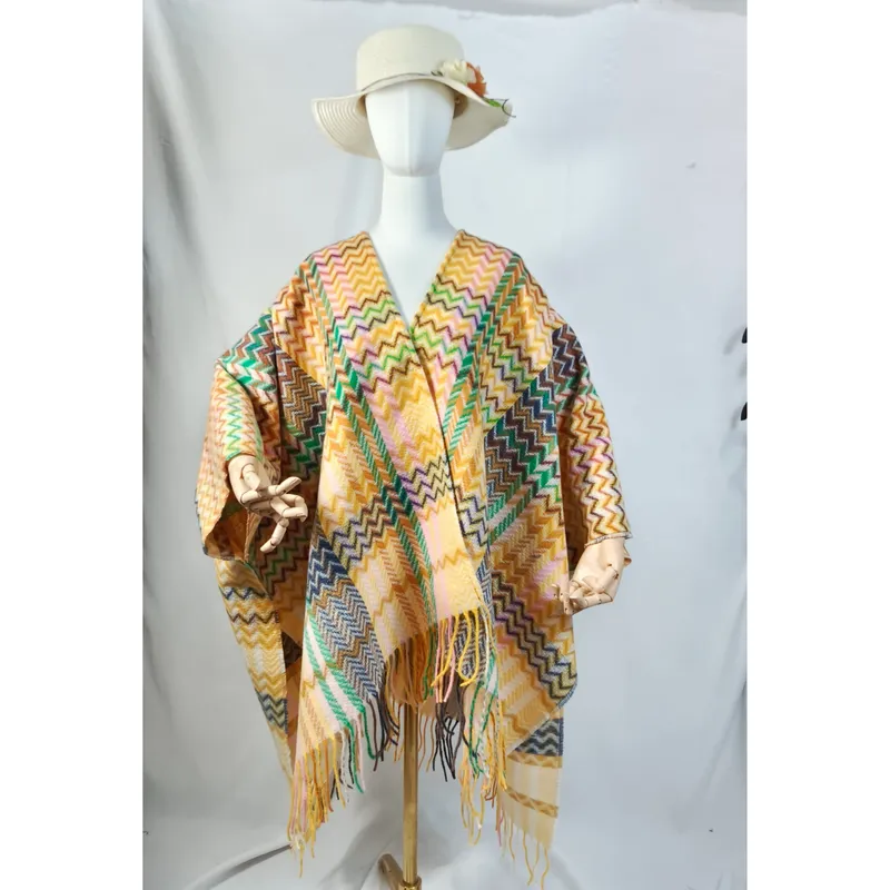 Modell trägt gemusterten Überwurfponcho mit Zickzack-Webmuster, Fransenabschluss und cremefarbenem Sonnenhut, weißer Hintergrund