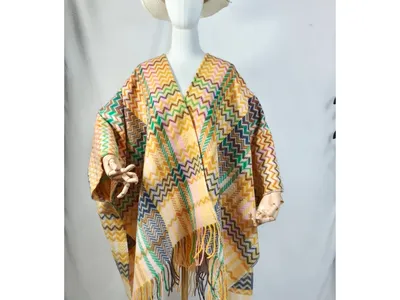 Modell trägt gemusterten Überwurfponcho mit Zickzack-Webmuster, Fransenabschluss und cremefarbenem Sonnenhut, weißer Hintergrund