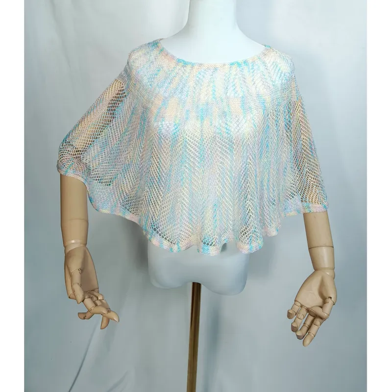 Weiße Schaufensterpuppe mit halbtransparentem Netzponcho in zarten Pastelltönen Hellblau, Pfirsich und Elfenbein, locker drapiert