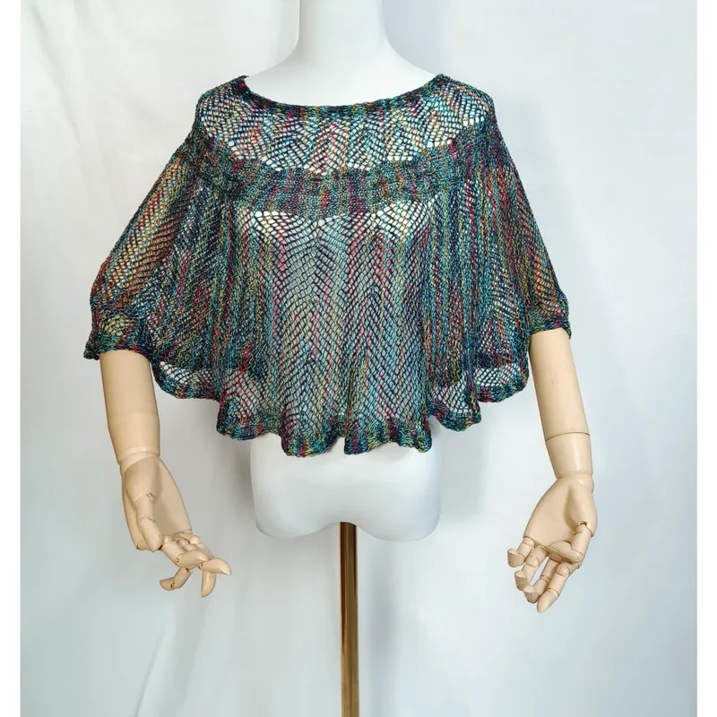 Mehrfarbiger Häkelponcho mit offenem Webmuster auf Schaufensterpuppe mit gegliederten Holzhänden, Regenbogen-Mesh-Stil