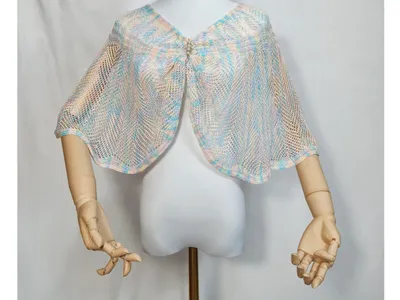 Offener Strickumhang in zartem Blau, Rosa und Creme mit glitzernder Strassbrosche auf weißer Schneiderpuppe