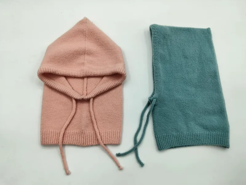 Zwei gestrickte Baby-Sturmhauben flach ausgelegt – eine in Altrosa geöffnet und eine in Petrol gefaltet, beide mit Kordelverschluss
