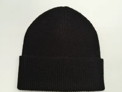 Schwarze Rippstrickmütze mit breitem umgeschlagenem Rand flach auf weißem Untergrund, weiche Wintermütze