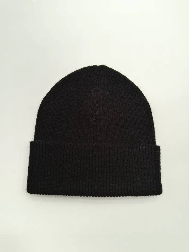 Schwarze Rippstrickmütze mit breitem umgeschlagenem Rand flach auf weißem Untergrund, weiche Wintermütze