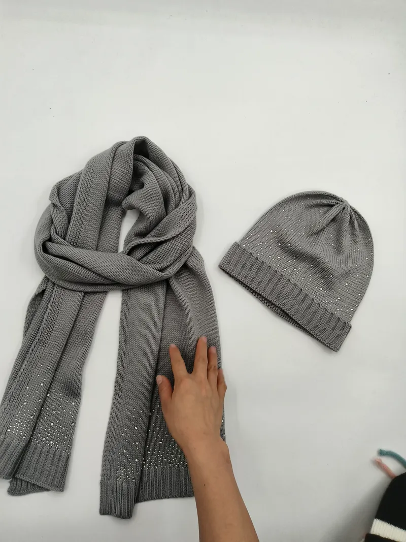 Graues Strickschal und Beanie-Set mit silbernen Strasssteinen auf weißer Fläche flach ausgelegt