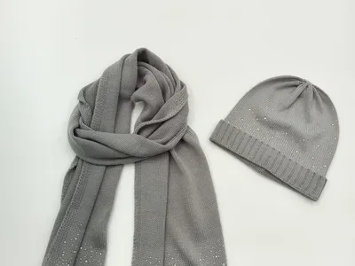 Graue Strickmütze und langer Schal mit funkelenden Kristallapplikationen auf weißem Hintergrund