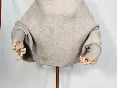Weiter cremefarbener Ajour-Strickpullover mit ausgestellten Ärmeln und Rautenmuster auf Schneiderpuppe mit Holzkünstlerhänden