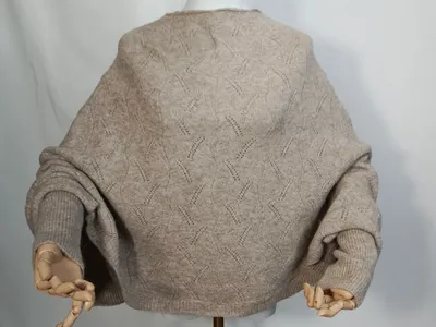 Rückenansicht eines weiten cremefarbenen Ajour-Strickpullovers mit Ballonärmeln und Rippbündchen auf weißer Schneiderpuppe