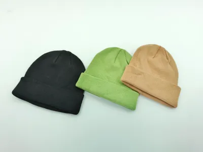 Drei schlichte Umschlag-Beanies flach liegend in Schwarz, Olivgrün und Hellbraun auf weißem Untergrund