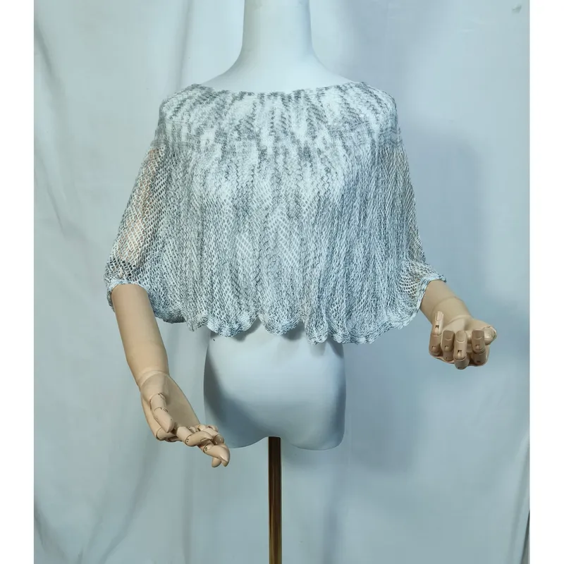 Kurzer Damen-Poncho aus grau-weißem Lochstrick auf Schaufensterpuppe, Bogensaum-Detail, leicht und transparent