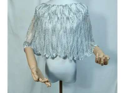 Kurzer Damen-Poncho aus grau-weißem Lochstrick auf Schaufensterpuppe, Bogensaum-Detail, leicht und transparent