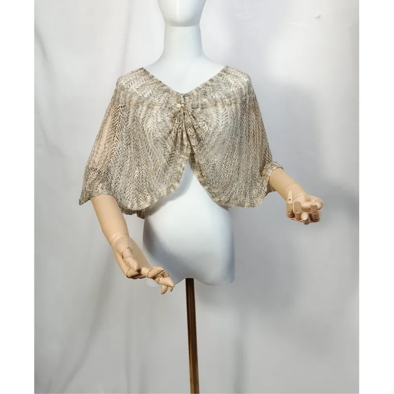 Offener Häkelumhang in Beige und Gold mit Zierknoten-Bindung, auf weißer Schaufensterpuppe, Bogensaum und Holzarme sichtbar