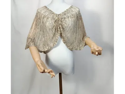 Offener Häkelumhang in Beige und Gold mit Zierknoten-Bindung, auf weißer Schaufensterpuppe, Bogensaum und Holzarme sichtbar
