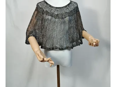 Kurzgeschnittener Metallicponcho in Silber und Schwarz auf weißer Schaufensterpuppe, weite Fledermausärmel, gelenkartige Holzarme