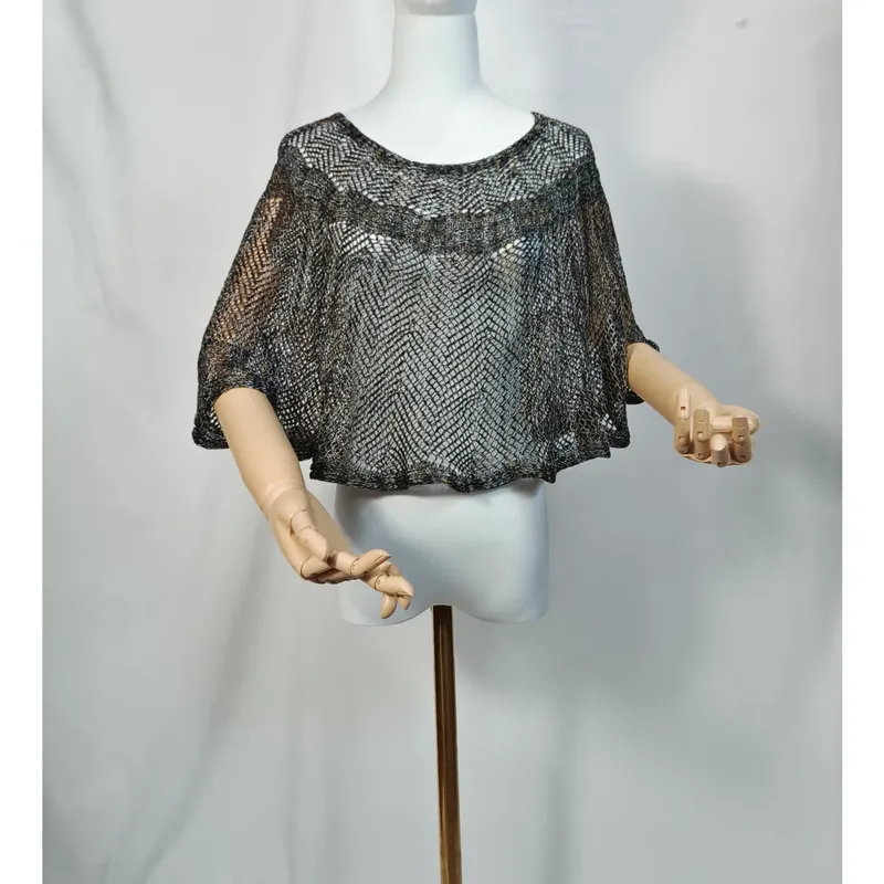 Kurzgeschnittener Metallicponcho in Silber und Schwarz auf weißer Schaufensterpuppe, weite Fledermausärmel, gelenkartige Holzarme