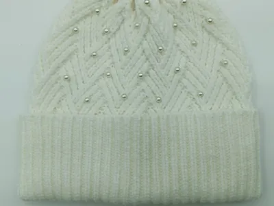 Weiche Wintermütze in Weißcreme mit Flechtmuster und aufgenähten Perlen als modisches Accessoire auf hellem Untergrund
