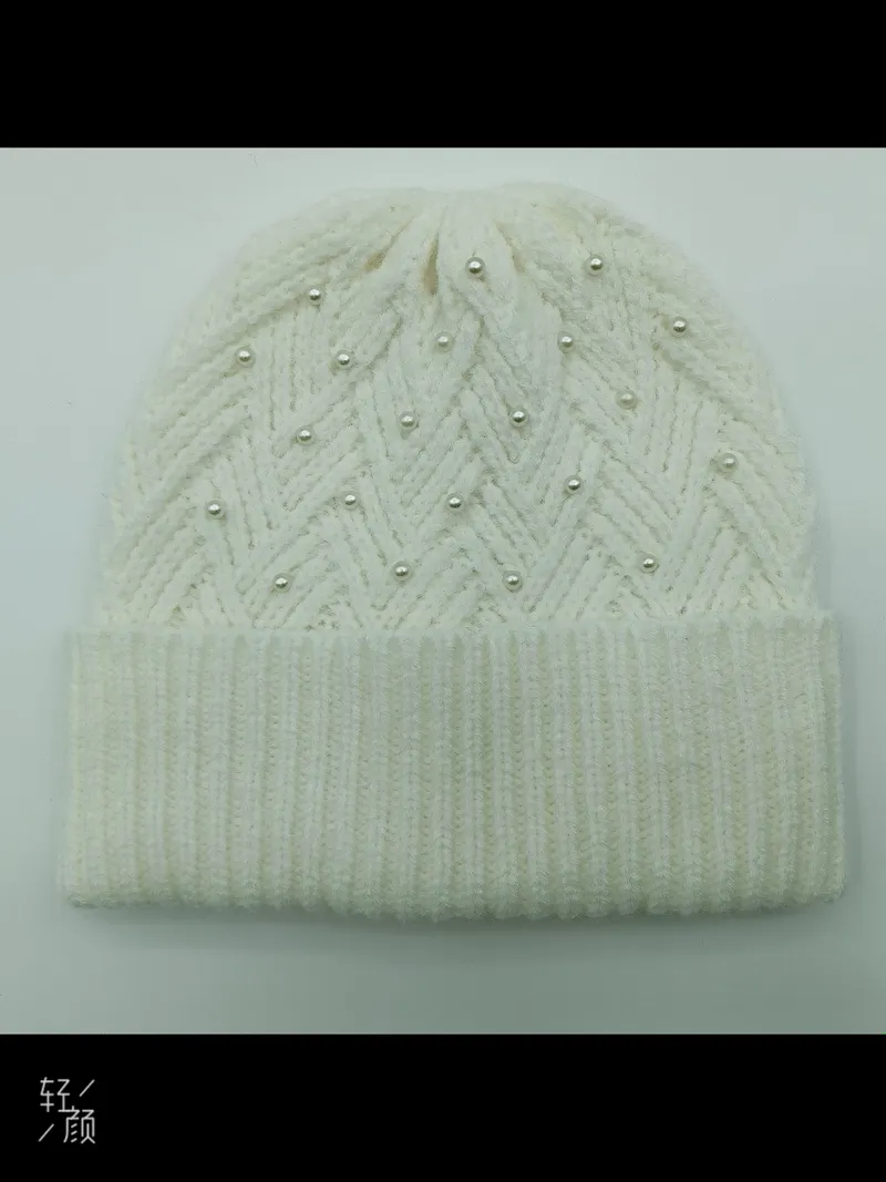 Weiche Wintermütze in Weißcreme mit Flechtmuster und aufgenähten Perlen als modisches Accessoire auf hellem Untergrund