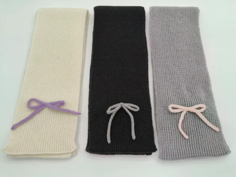Drei elegante Strickschals in Creme, Anthrazit und Hellgrau mit dekorativer Garnschleife, glatt auf hellem Untergrund fotografiert