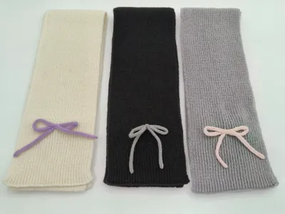 Drei elegante Strickschals in Creme, Anthrazit und Hellgrau mit dekorativer Garnschleife, glatt auf hellem Untergrund fotografiert