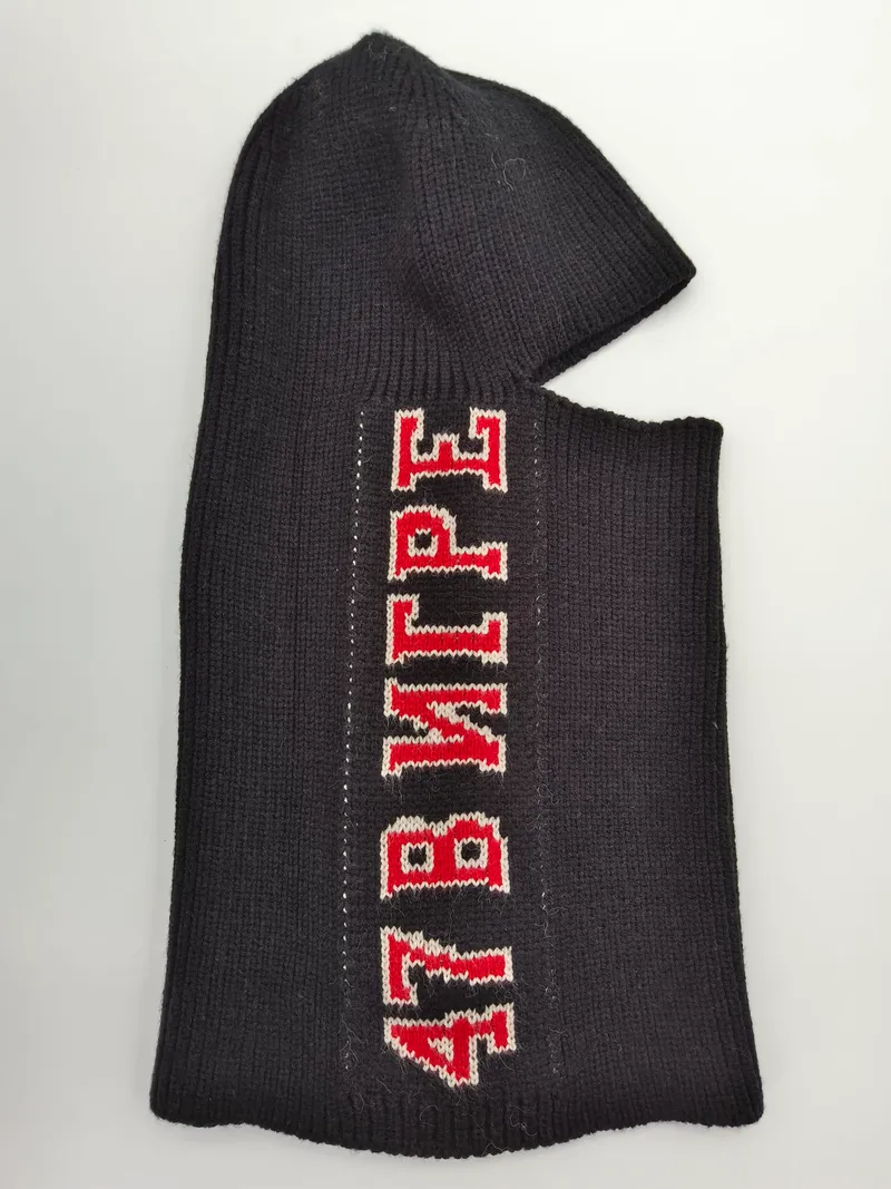 Schwarze Rippenstruktur-Skimaske flach präsentiert mit rot-weißem Varsity-Letter-Aufdruck auf dunklem Strickgewebe