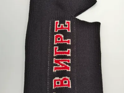 Schwarze Rippenstruktur-Skimaske flach präsentiert mit rot-weißem Varsity-Letter-Aufdruck auf dunklem Strickgewebe